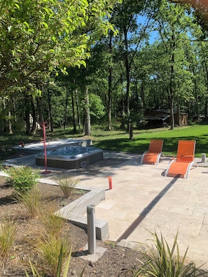 Un bain à remous entouré de chaises longues orange, une terrasse en bois et une zone herbeuse avec des arbres.