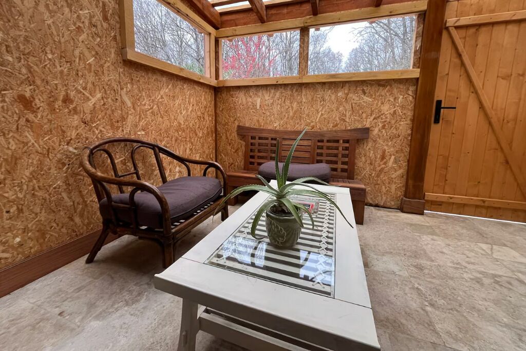 Een kamer met een houten wand, een glazen tafel met een plant, een fauteuil en een bank.