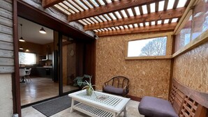 Una habitación con techo de madera, una ventana, una mesa blanca con una planta, un banco acolchado y vistas a la cocina.