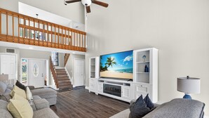 Un salón amplio con una gran televisión de pantalla plana, una escalera y un balcón.