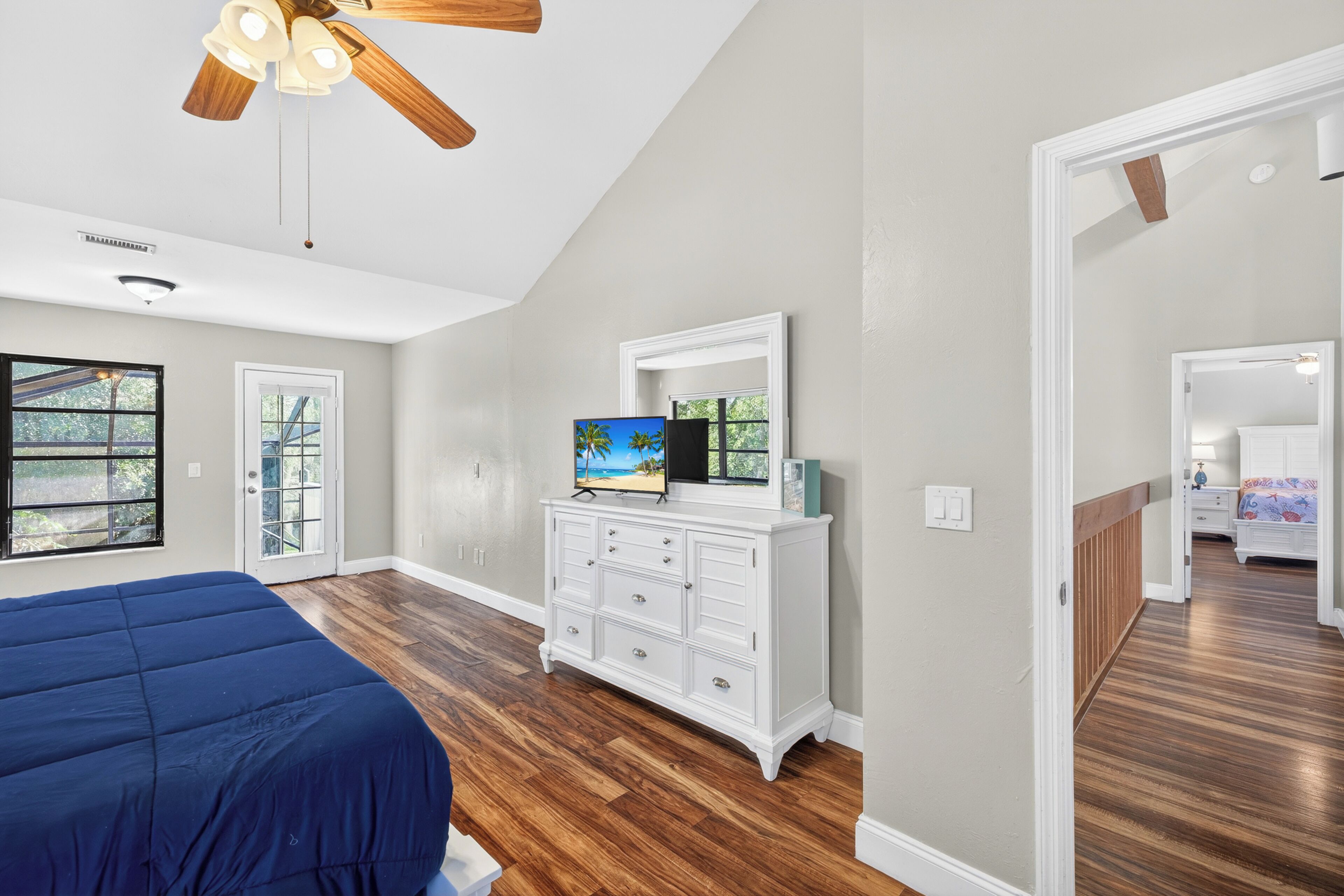 Une chambre à coucher avec un lit, une commode, un ventilateur de plafond et une grande fenêtre.