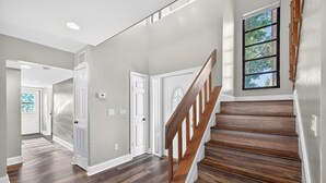 Un pasillo con piso de madera, puertas blancas y una escalera de madera.