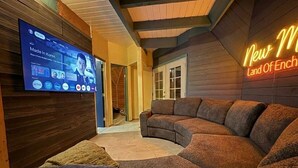 Uma sala de estar moderna com um sofá seccional curvo, uma TV de tela plana na parede e uma luminária de neon com a inscrição 'New World Land Of Ench'.
