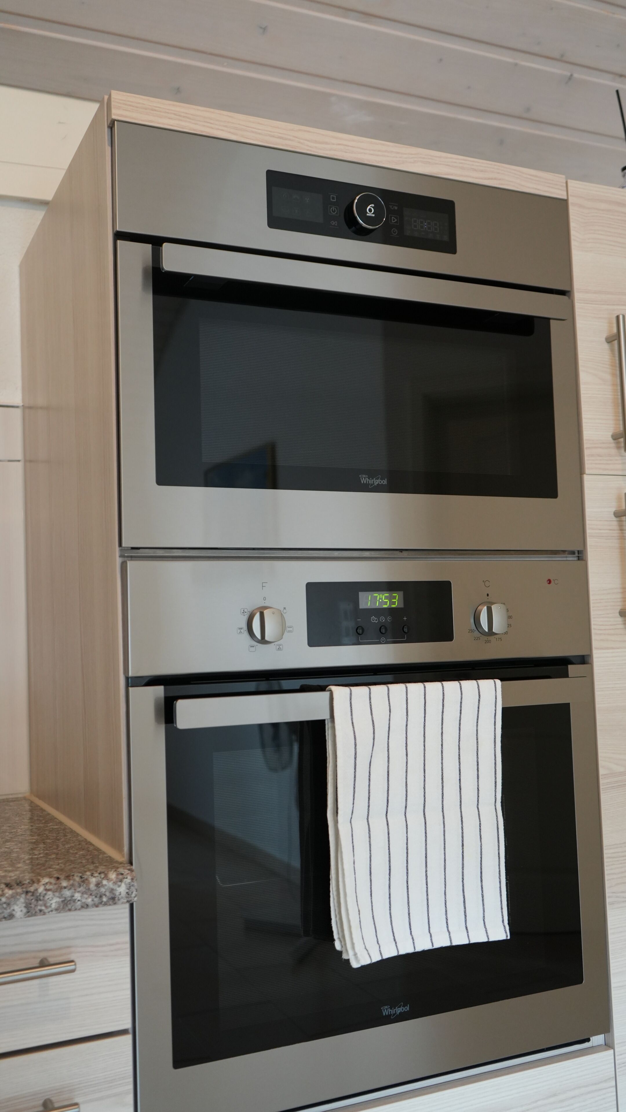 En stålfarvet Whirlpool ovn med digitalt ur, kontrolpanel og et håndklæde hængende på døren.
