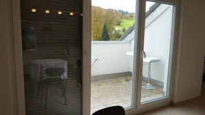 A room with a sliding glass door leading to a balcony with a table and chairs, and a white sink. - Delightful 1-bedroom apartment in Safenwil perfect for your stay (Safenwil)