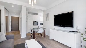 Ein modernes Wohnzimmer mit einer Couch, einem Glastisch und einem an einer weißen Kommode befestigten Fernseher.