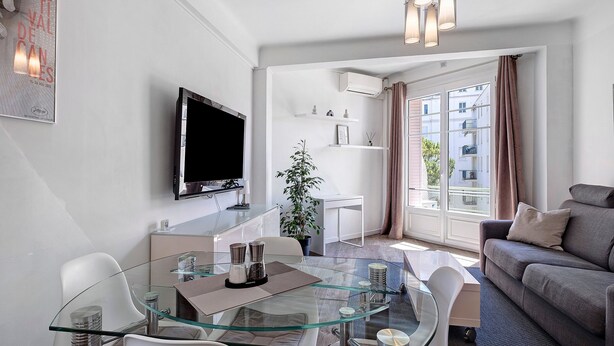 Ein modernes Wohnzimmer mit einem Glastisch, einer Couch, einem Flachbildfernseher und einem großen Fenster mit Vorhängen.