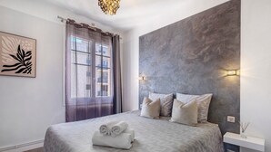 Ein modernes Schlafzimmer mit einem großen Bett, einem Fenster mit Vorhängen, einer Wandleuchte und einem Gemälde.