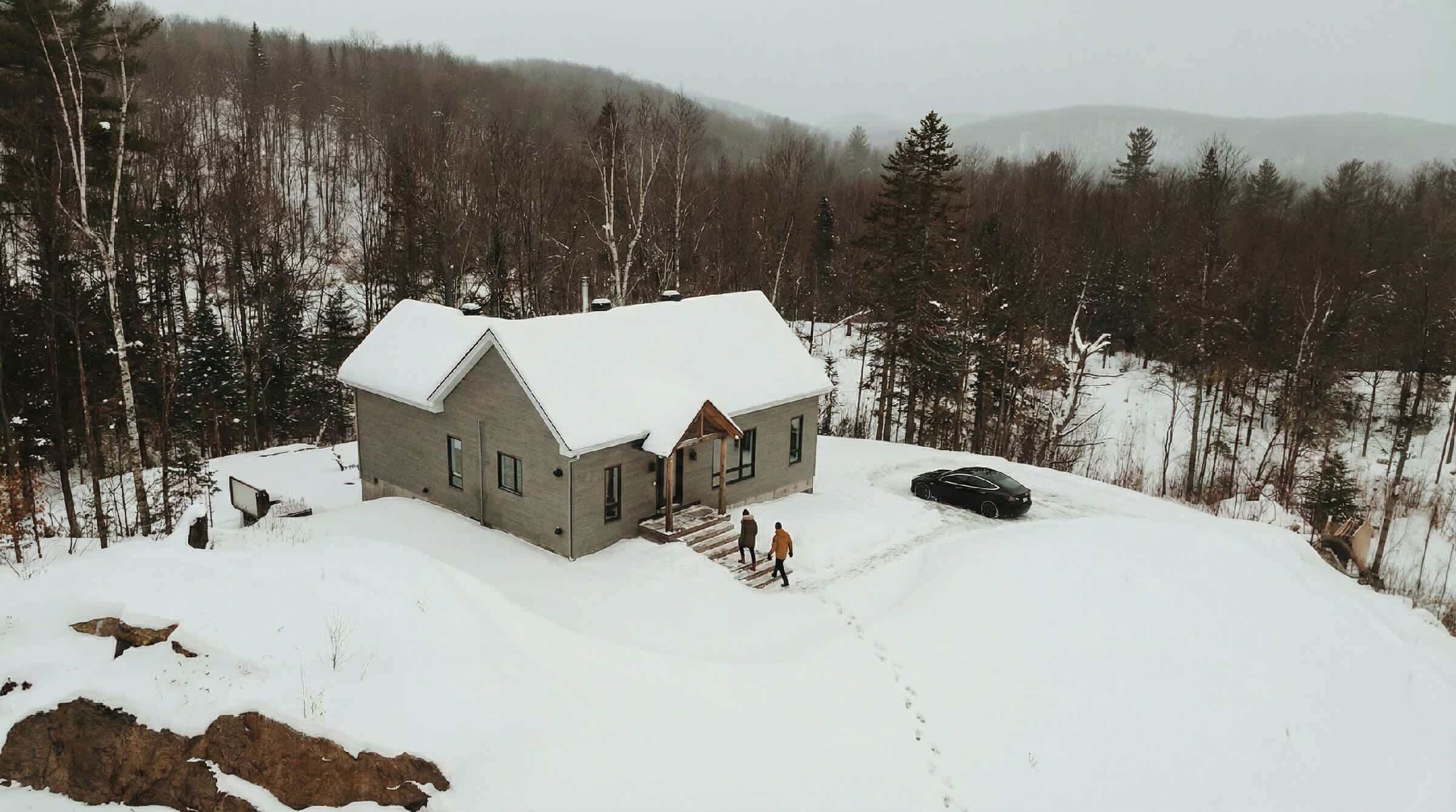 Una casa con tejado nevado, un porche y un coche estacionado al frente.