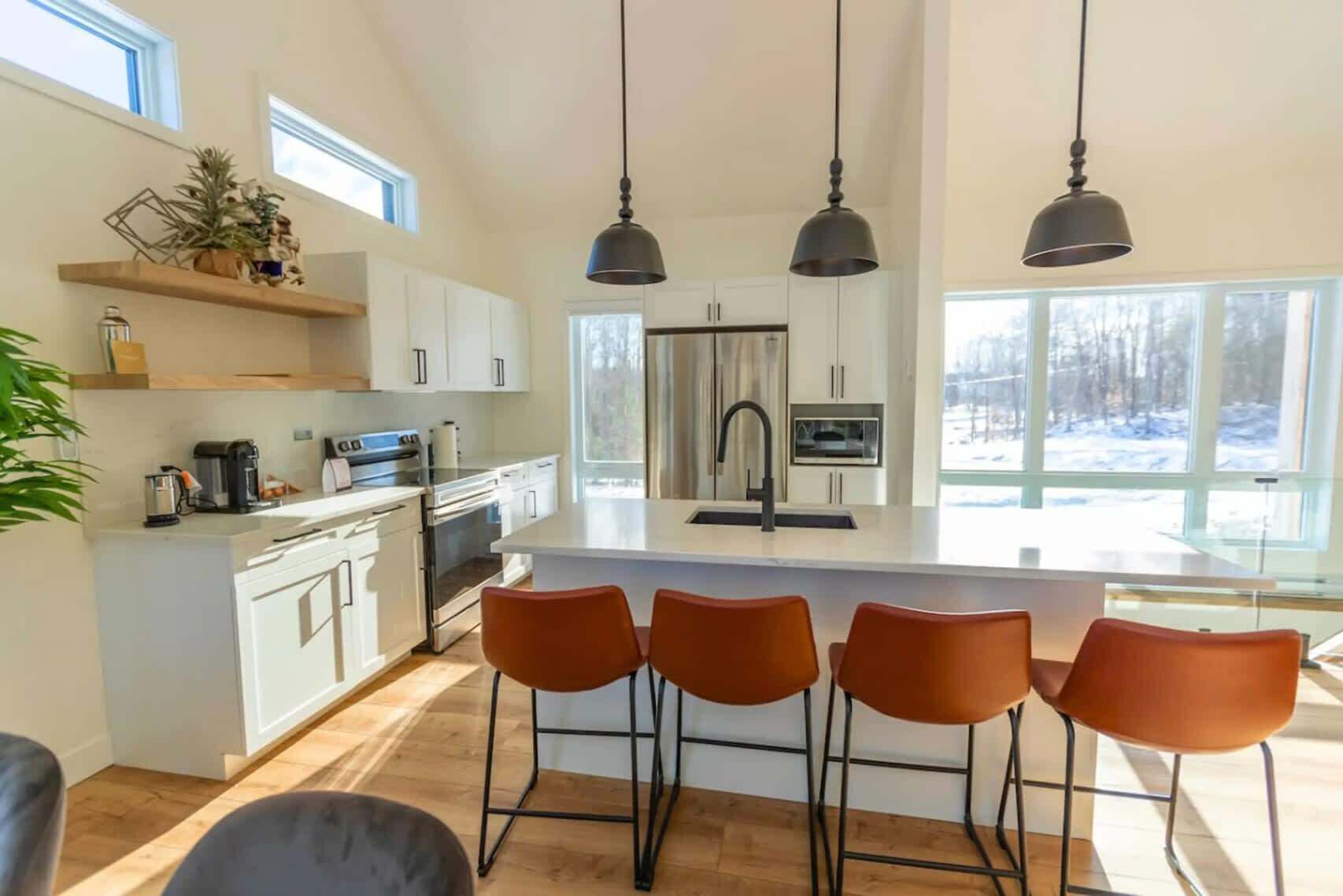 Une cuisine moderne avec des meubles blancs, un îlot central, des tabourets de bar et des luminaires suspendus.
