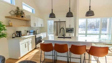 Une cuisine moderne avec des meubles blancs, un îlot central, des tabourets de bar et des luminaires suspendus.