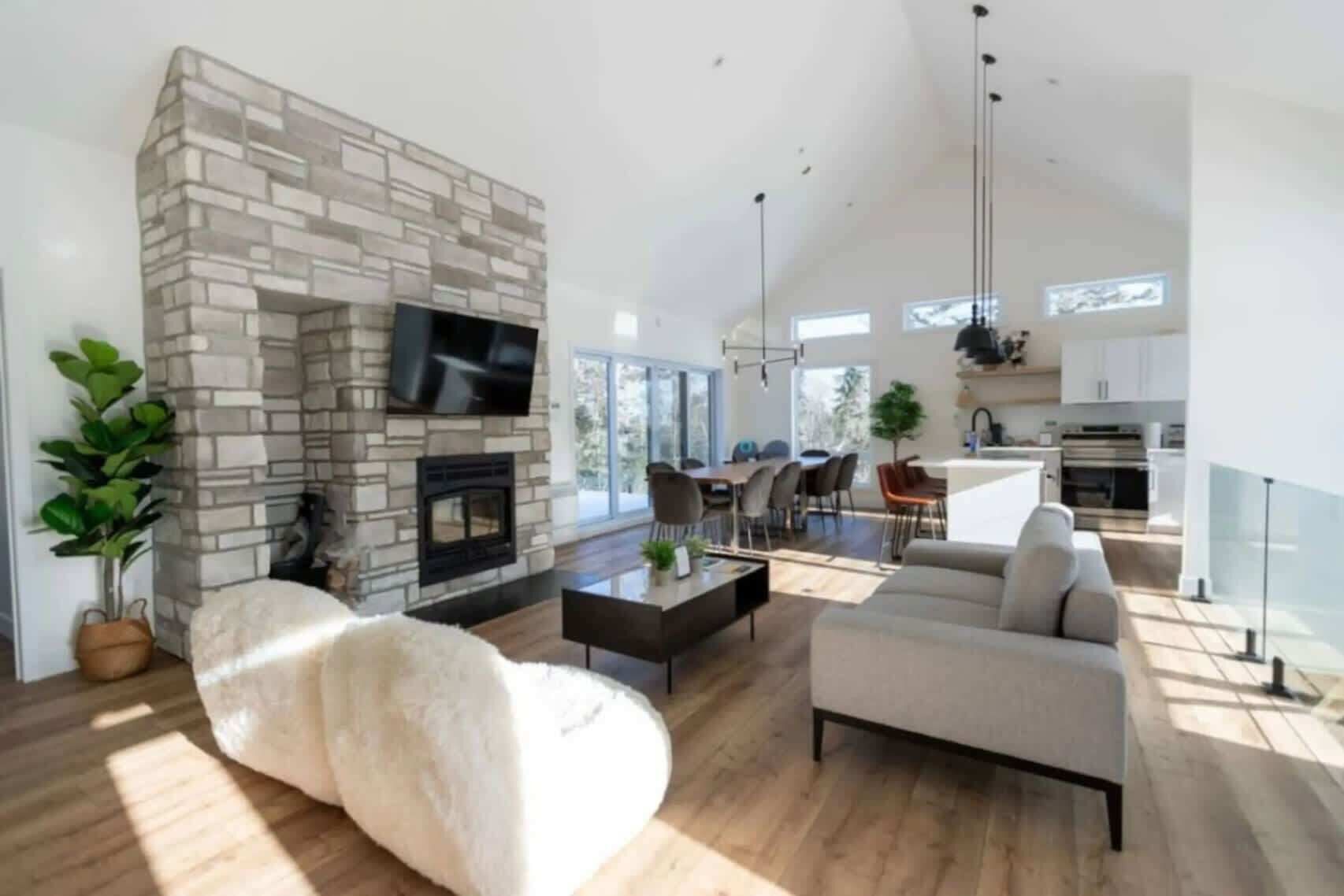 A modern living room with a stone fireplace, a flat-screen TV, a sofa, and a dining area with chairs.