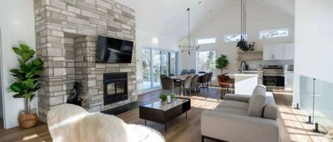 A modern living room with a stone fireplace, a flat-screen TV, a sofa, and a dining area with chairs.