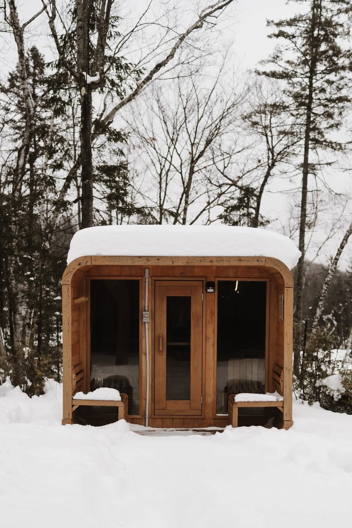 Une cabane en bois avec une porte et des fenêtres, entourée de neige et d’arbres.