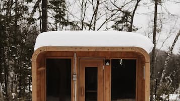 Une cabane en bois avec une porte et des fenêtres, entourée de neige et d’arbres.