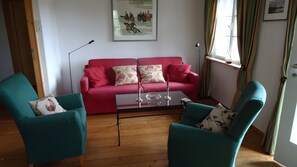 A living room with a red sofa, teal armchairs, a glass coffee table, and a painting on the wall.