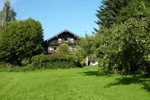 Ein zweistöckiges Haus mit Balkon, umgeben von üppigem Grün und Bäumen.