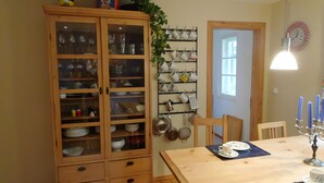 A dining area with a wooden cabinet, a wall-mounted utensil rack, a dining table with a placemat, and a candle holder.