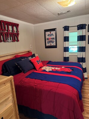A bedroom with a large bed, a wooden headboard, a framed picture on the wall, and a window with curtains.