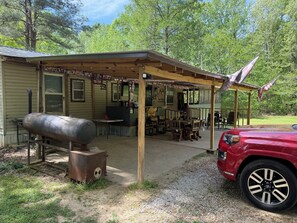 A rustic outdoor dining area with a covered patio, a grill, and a red SUV parked nearby.