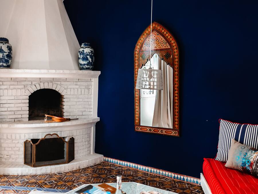 A room with a white brick fireplace, blue and white patterned tiles, a red sofa, and a large ornate mirror.