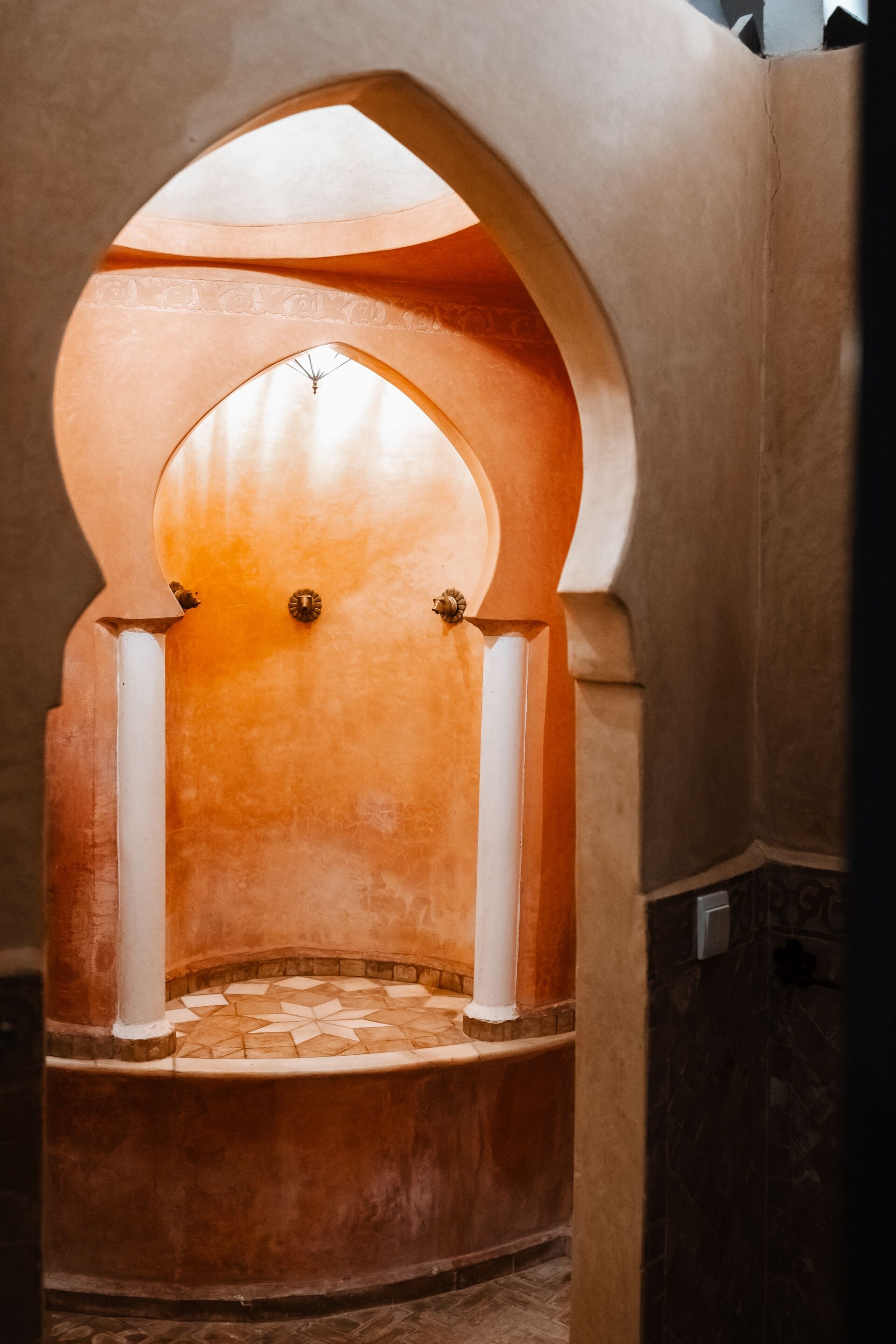 Un arco empotrado con suelo de baldosas, columnas blancas y pared de tonos cálidos.