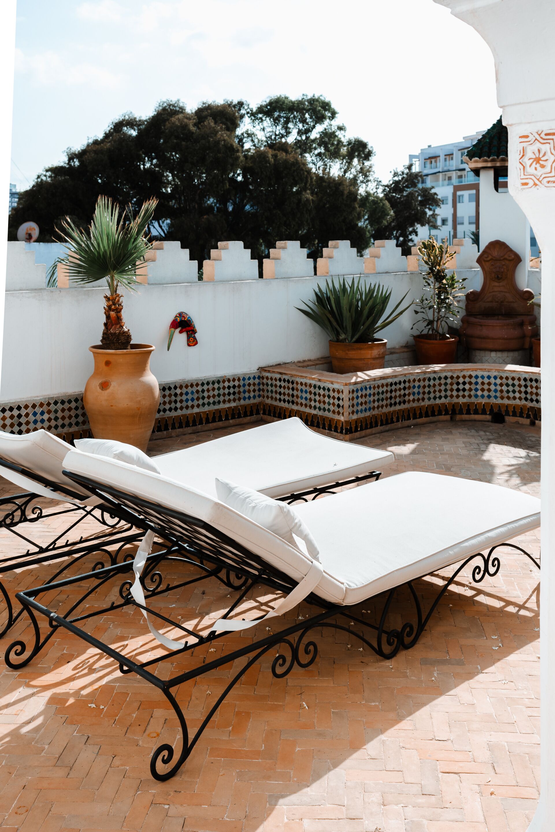 A rooftop terrace with lounge chairs, potted plants, and a tiled wall.