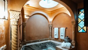 A spa room with a marble bathtub, a vanity with a mirror, and a large arched doorway. - Lalla Soulika (Tangier)