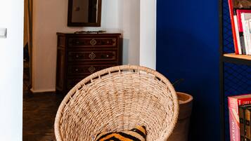 A room with a woven chair, a bookshelf, a tray with teapots and cups, and a patterned rug.