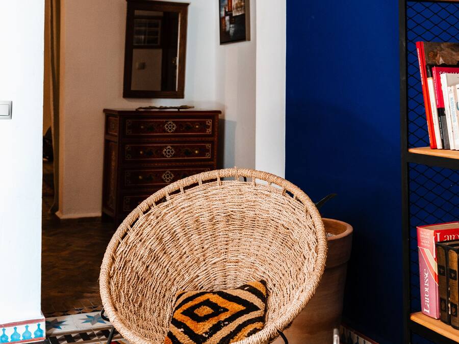 A room with a woven chair, a bookshelf, a tray with teapots and cups, and a patterned rug.