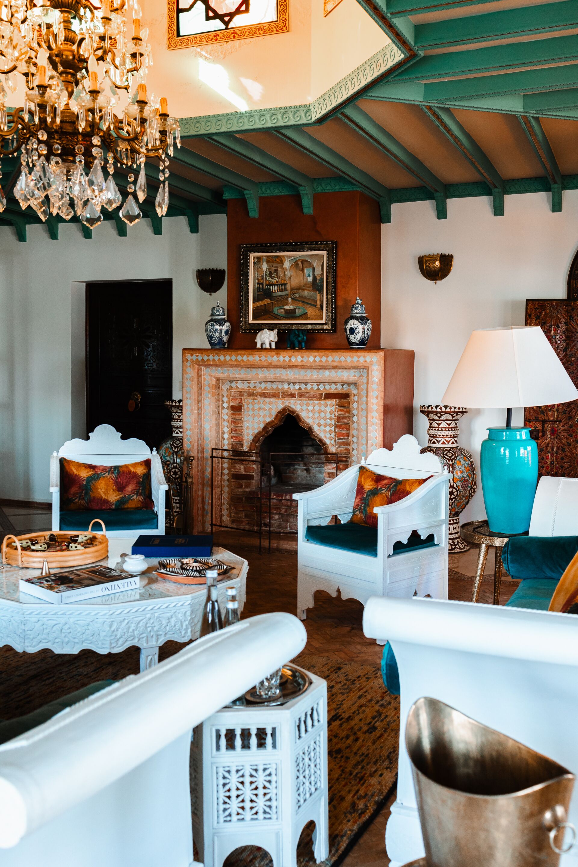 A room with a fireplace, white furniture, a chandelier, and a patterned rug.