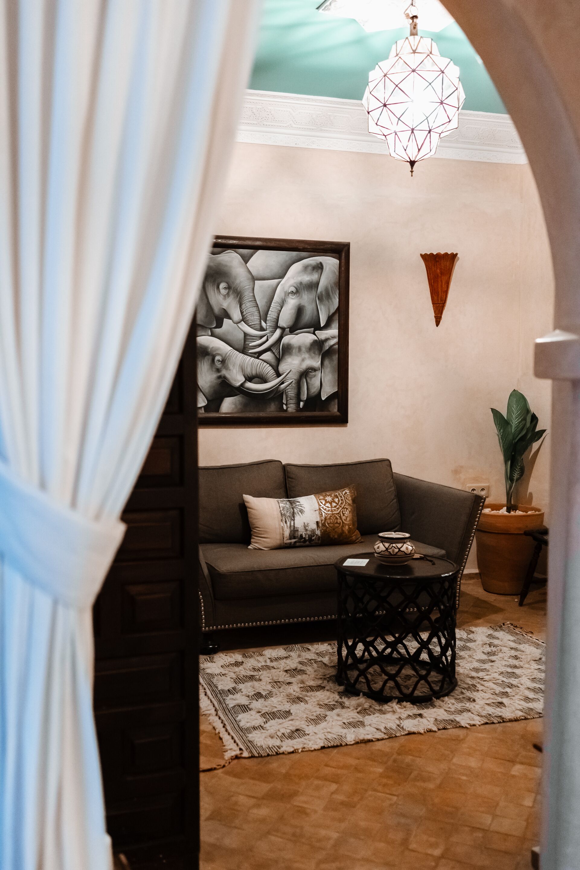 A cozy living area with a sofa, a decorative wall piece, a hanging light fixture, and a potted plant.