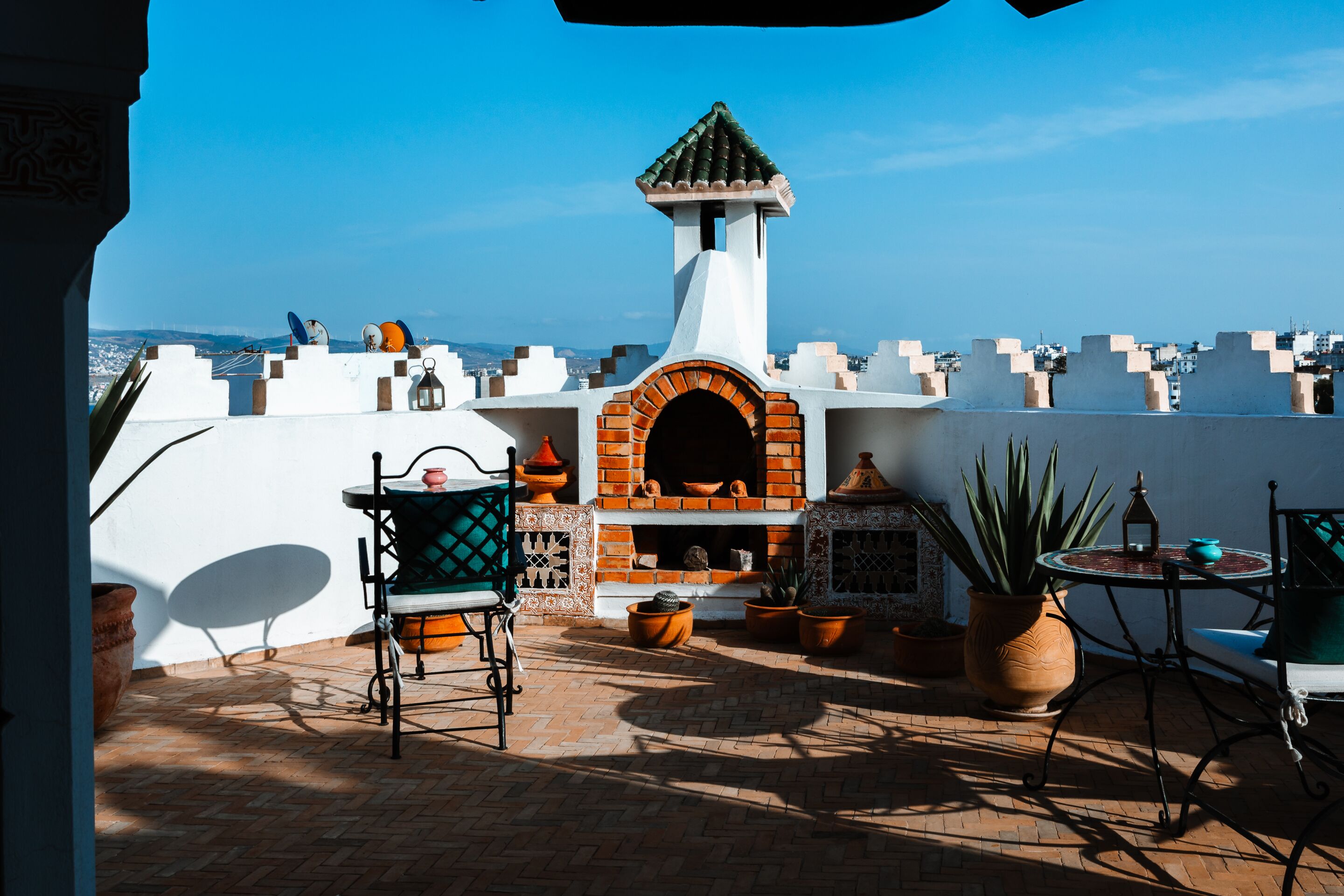 A rooftop patio with a brick oven, potted plants, and outdoor furniture.