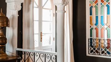 Une pièce dotée d’un sol à motifs, d’une porte en arc blanc, d’une fenêtre ornée de vitraux colorés et d’une rambarde en métal.