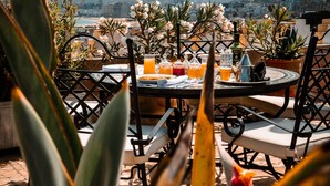 An outdoor dining area with a table set for two, surrounded by chairs, with a view of the city and hills in the background. - Lalla Soulika (Tangier)