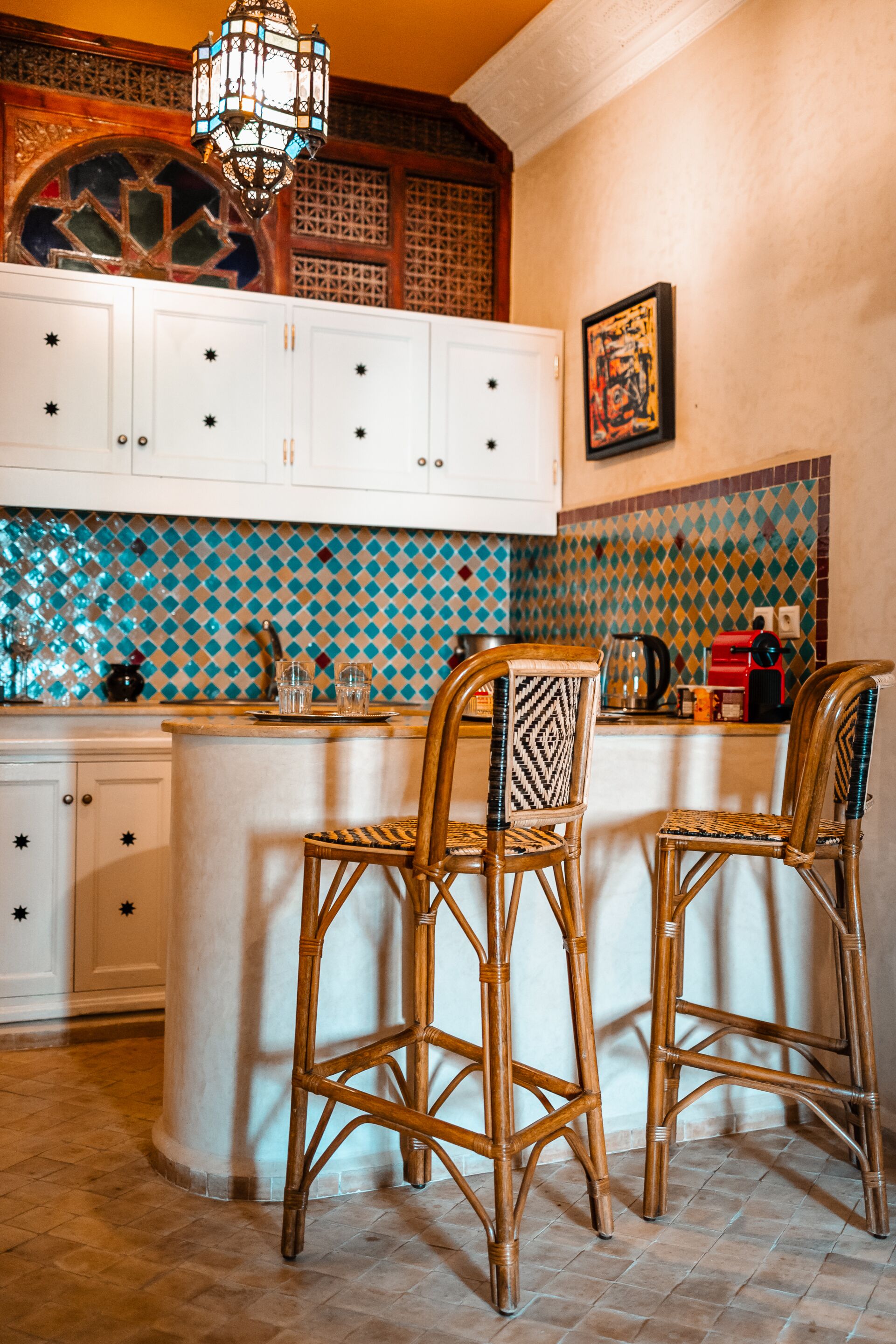 A kitchen with white cabinets, a patterned backsplash, and two wicker chairs at a bar area.