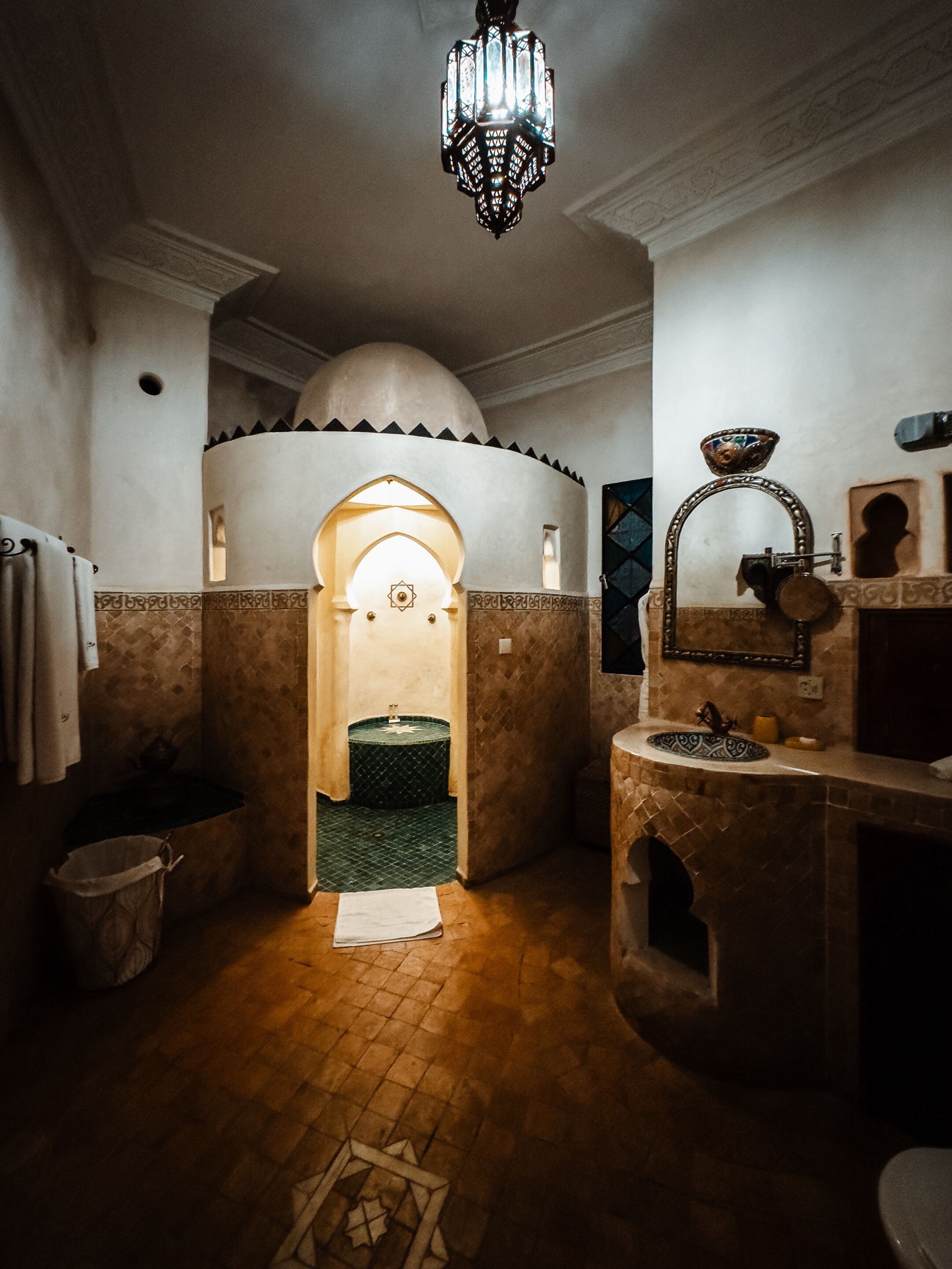 A traditional bathroom with a tiled floor, a sink, a mirror, and a hanging light fixture.