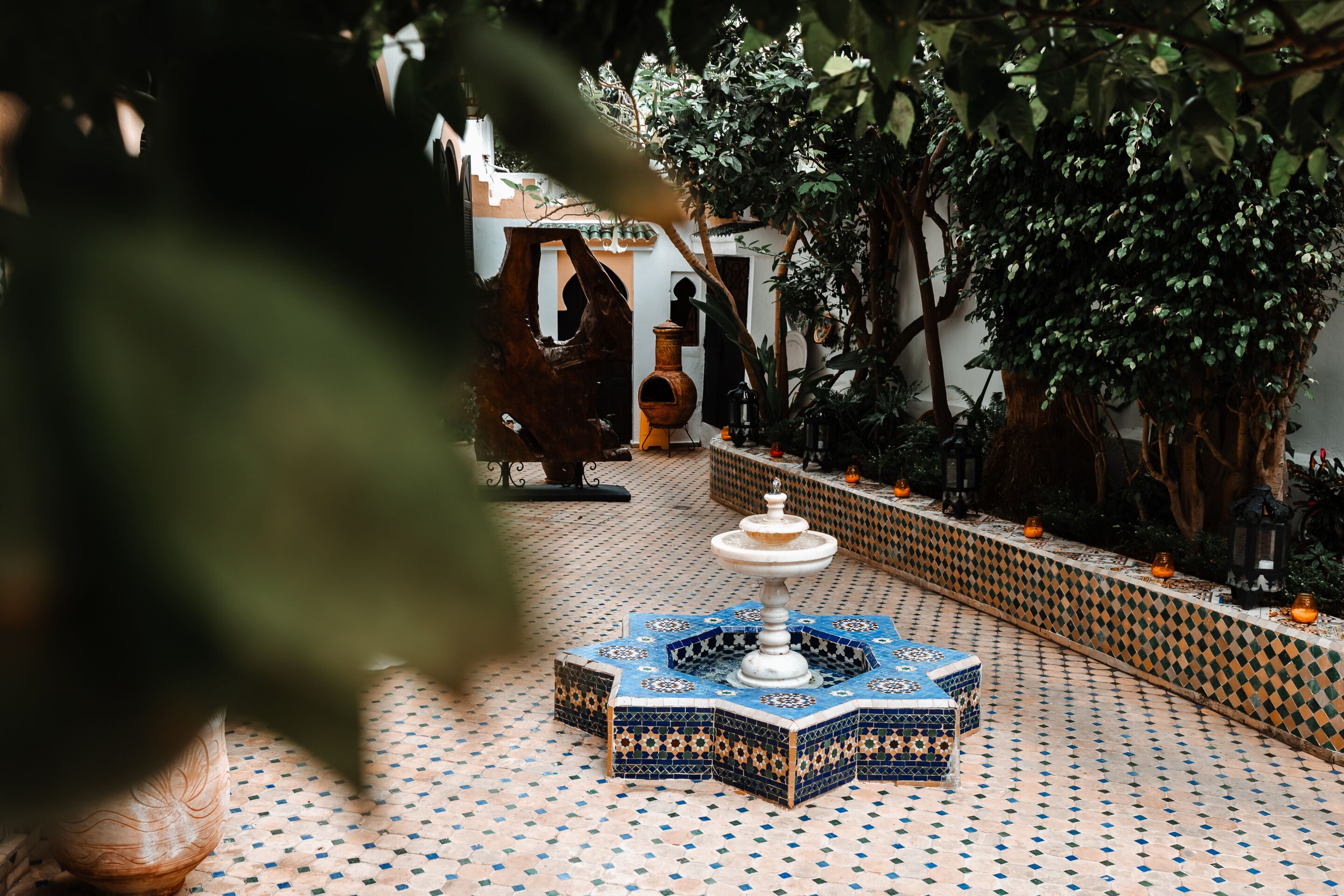 Un patio con una fuente, suelo de baldosas y plantas en macetas.