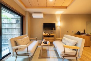 Habitació d'hotel moderna amb sofà, taula petita amb safata, televisió i escriptori amb làmpada.