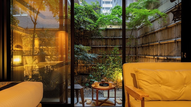 A room with a sliding glass door leading to a garden, a sofa, and a small table with cups. - Hotel Rakurakuan (Kyoto)