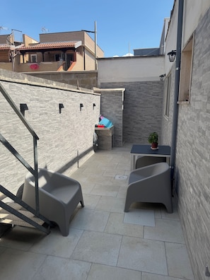 Una terrazza sul tetto con una scala, un tavolino con una pianta in vaso e una ringhiera in metallo.