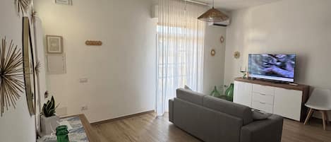 Una sala de estar con sofá, televisor y suelo de madera.