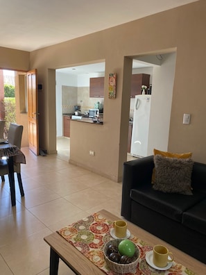 A living room with a sofa, a coffee table with decorative items, and a view into the kitchen.