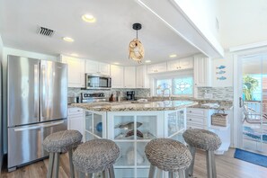 A modern kitchen with a stainless steel refrigerator, a microwave, and a built-in oven. There are three woven stools and a central island with a glass enclosure. - 🏖️Private Pool | Easy Beach Access | Great Outdoor Spaces | Into the Mystic🏖️ (Fort Myers Beach)