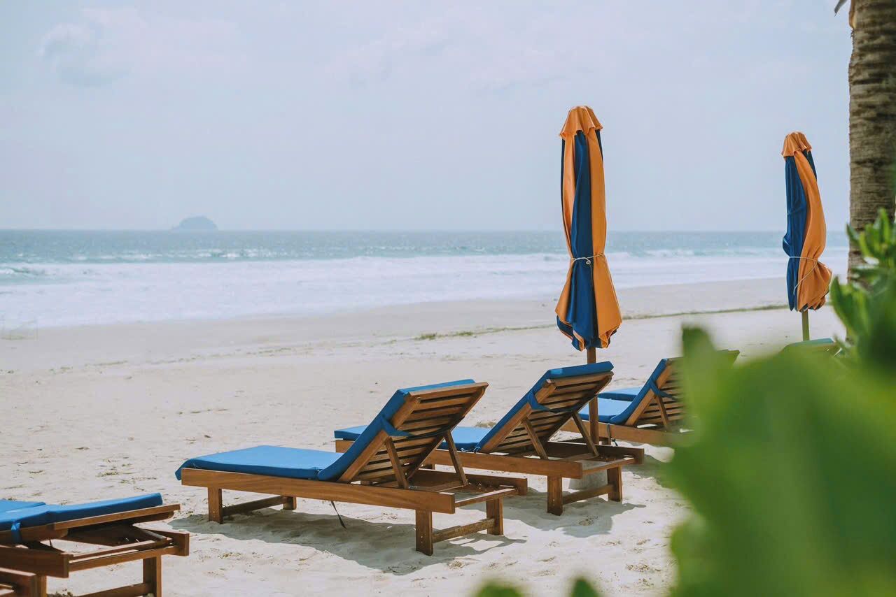 A beach with wooden lounge chairs and orange umbrellas.