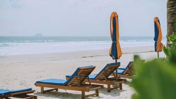 A beach with wooden lounge chairs and orange umbrellas.