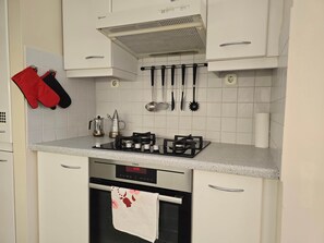 Una cucina con gas, forno e diversi utensili appesi al muro.