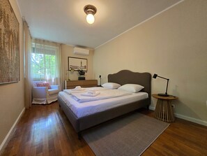 Quarto bem arrumado com cama, abajures, mesa de cabeceira e janela com cortinas.