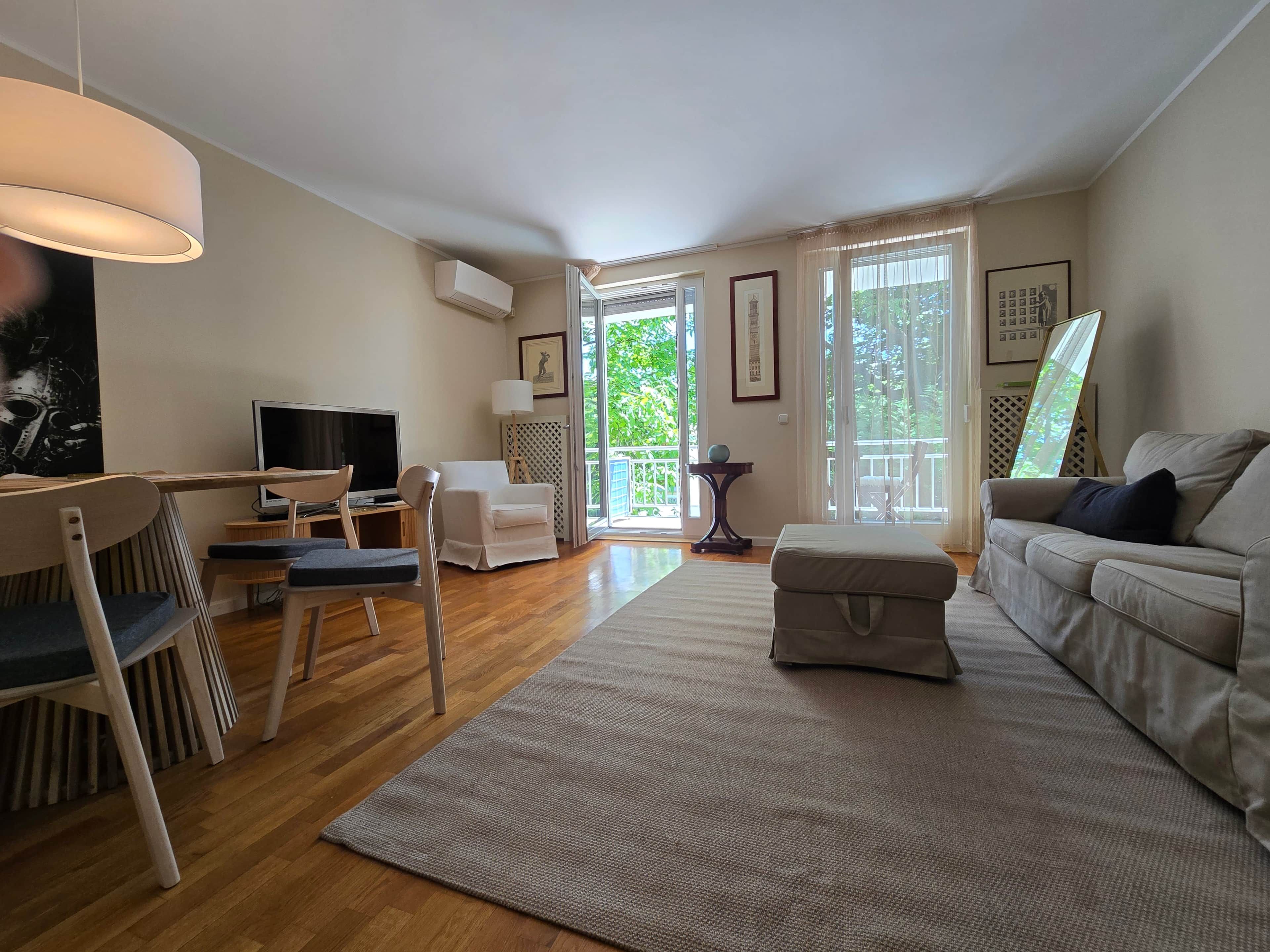 A living room with a television, seating, a sofa, a rug, and a balcony with a view.