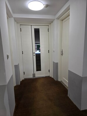Un passadís amb dues portes blanques, una d'elles amb un panell de vidre, i una làmpada al sostre.